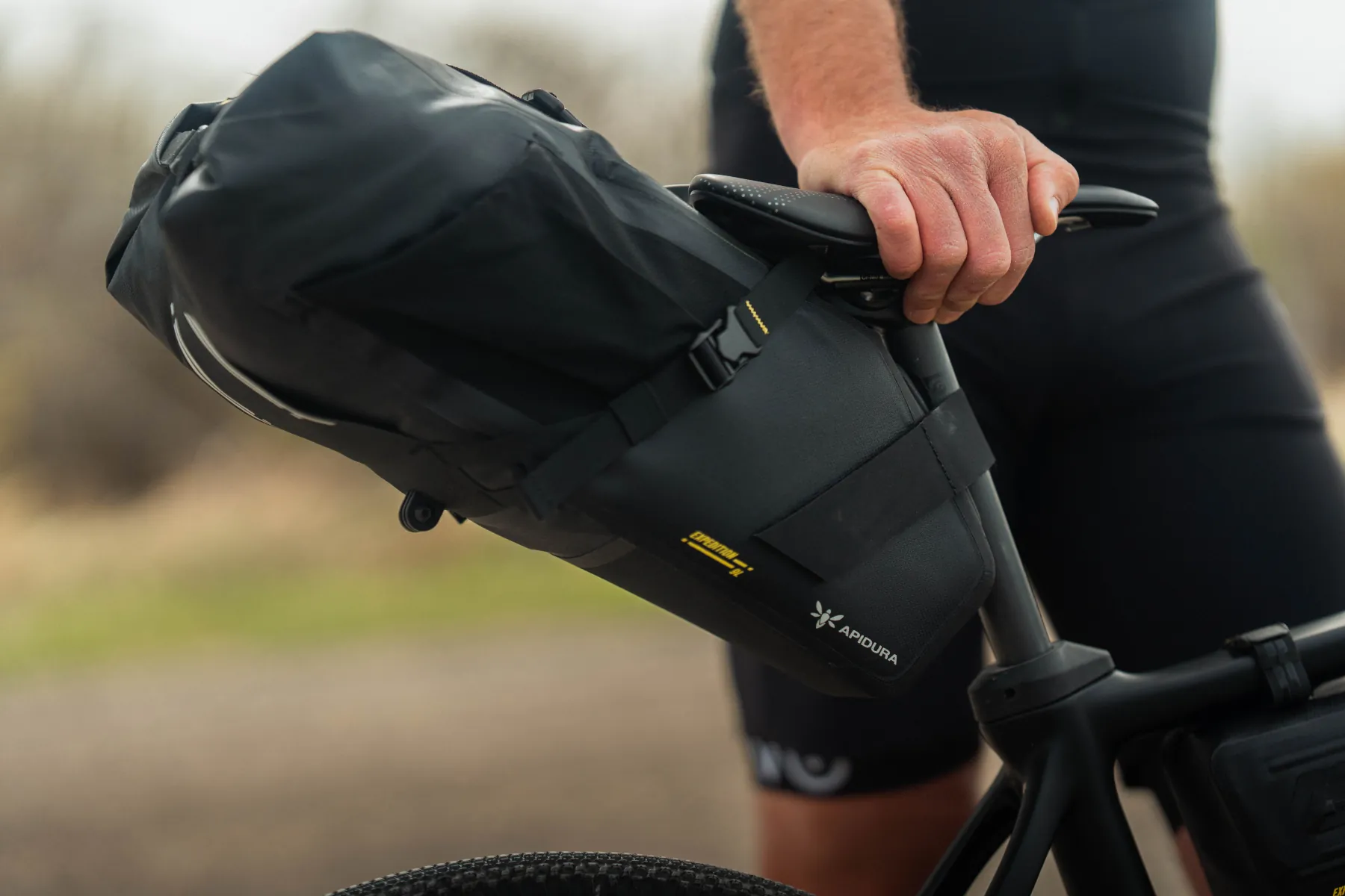 Rider's hand on the saddle beside a loaded Apidura Expedition saddle pack
