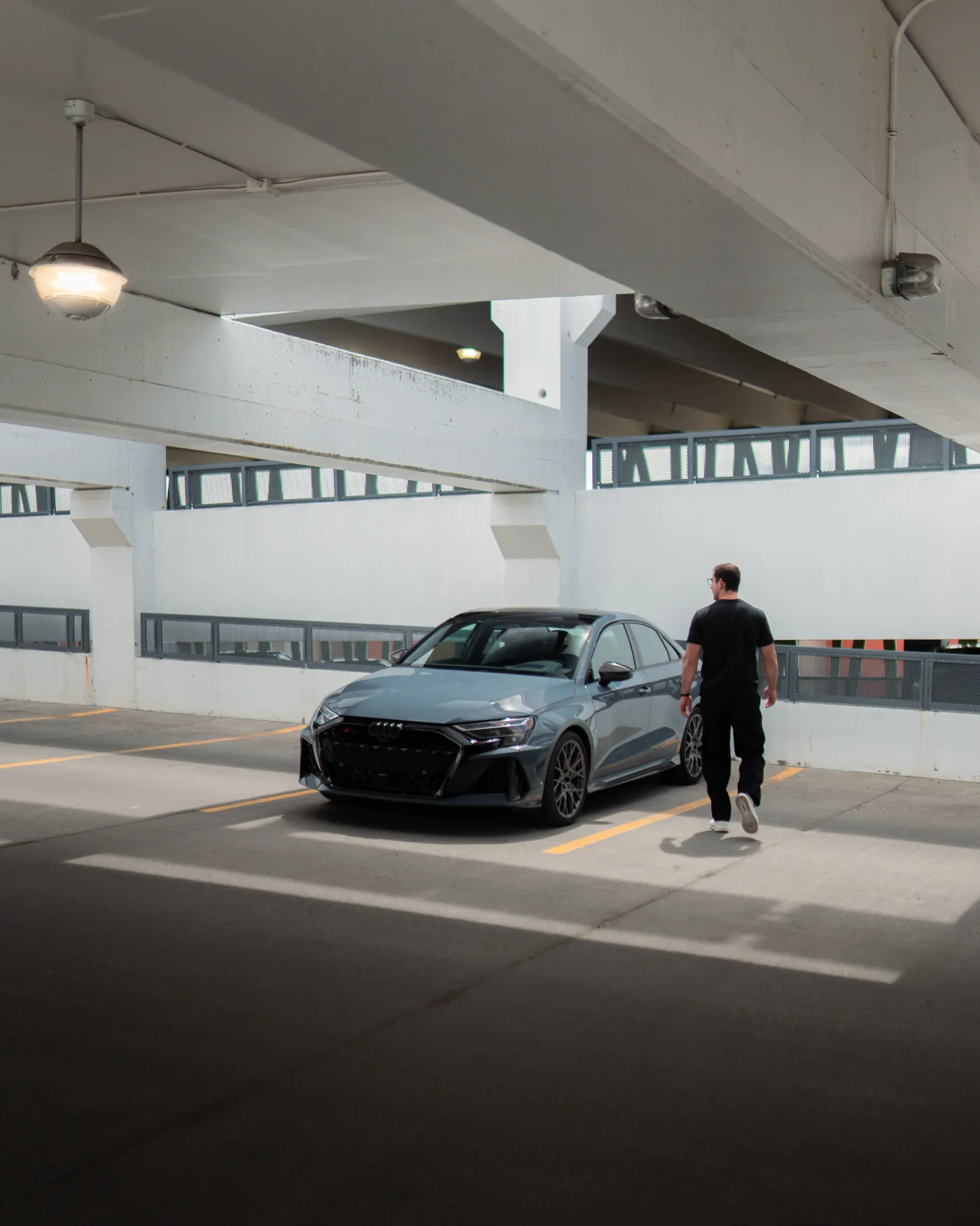 Audi RS3 parked in a white parking garage, driver at the front wing
