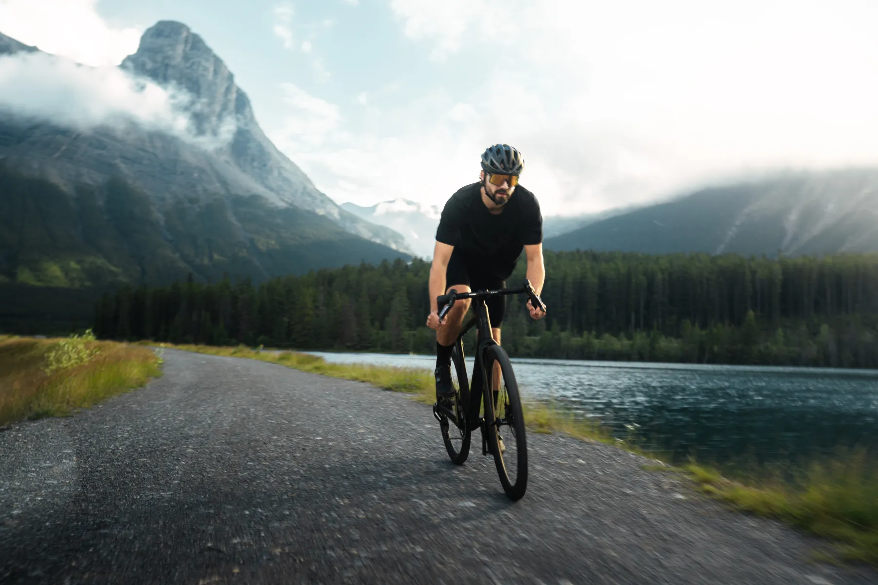 Cyclist riding a lakeside gravel path beneath a Rockies peak