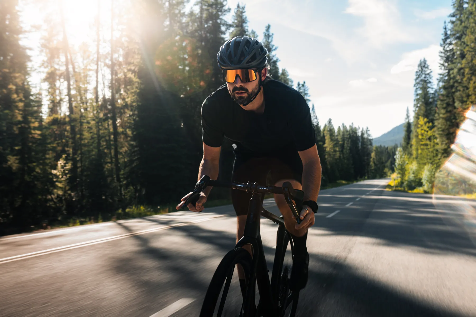 Rider on the Pivot climbing a sunlit forest road toward camera
