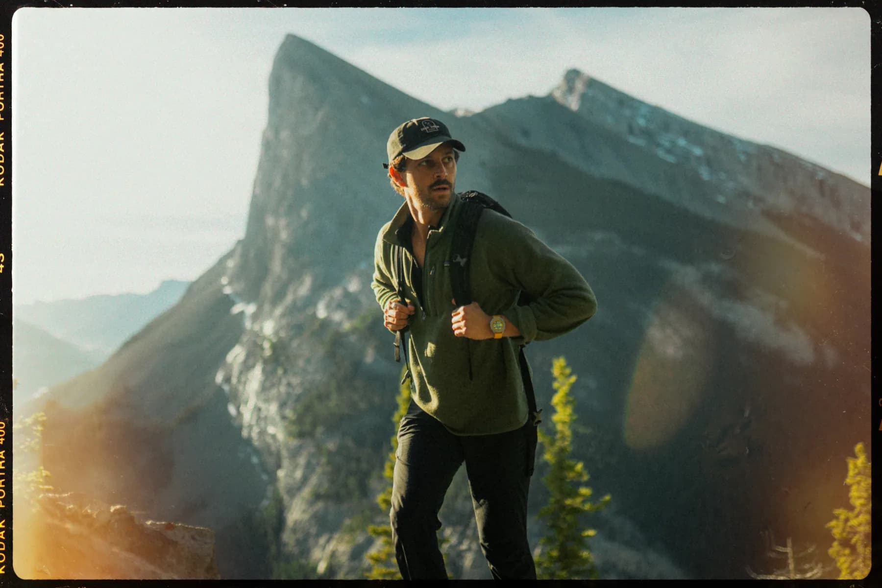 Hiker on a mountain ridge at golden hour wearing the RZE watch, shot on film