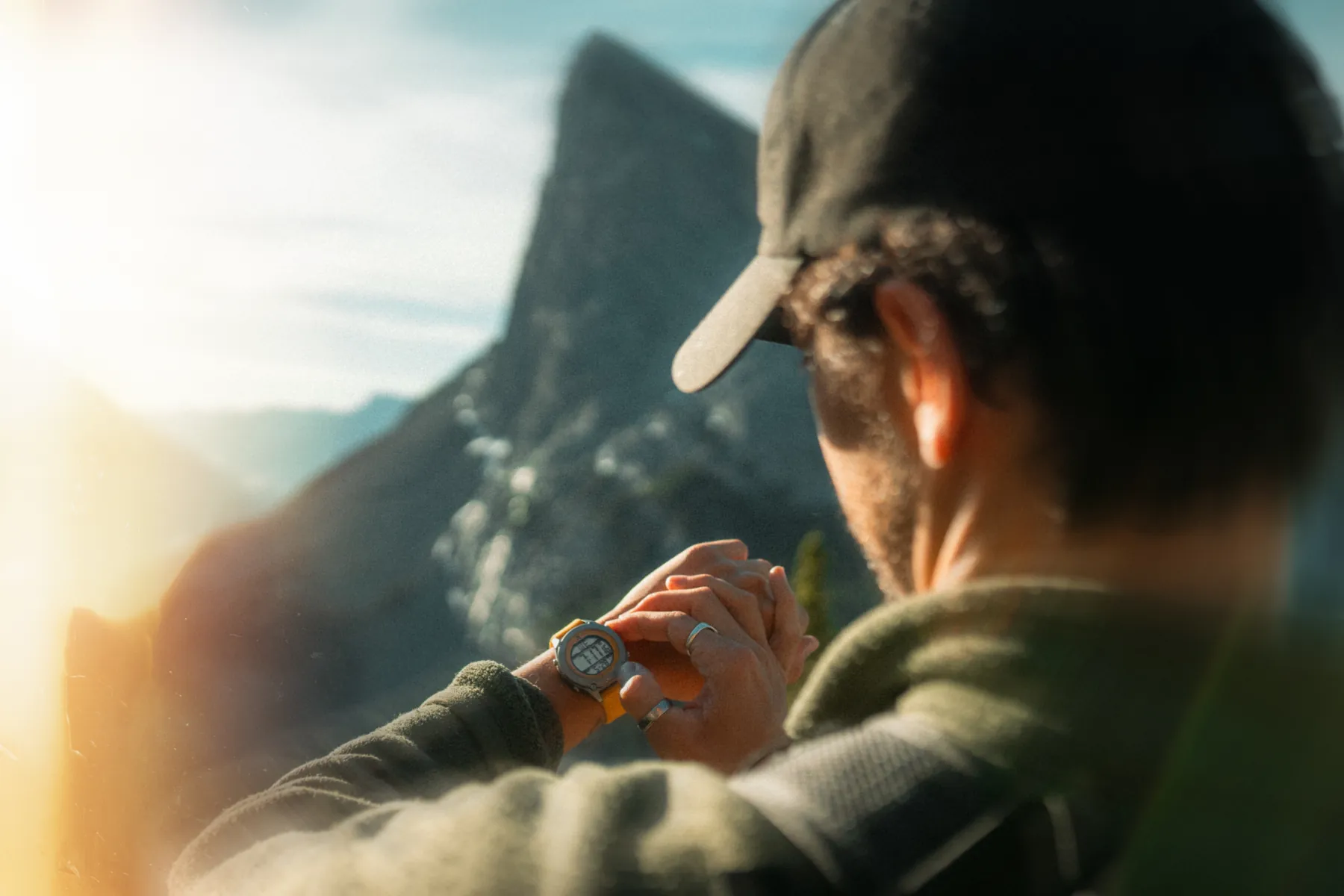 Hiker checking his RZE titanium watch at sunrise, summit behind